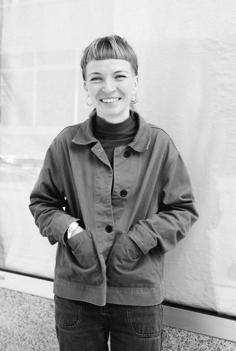 Miriam lächelt in die Kamera. Eine Frau mit Pony, die Hände in den Jackentaschen.